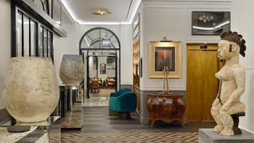 A lobby with a grand staircase, a large vase, a teal armchair, and a statue.