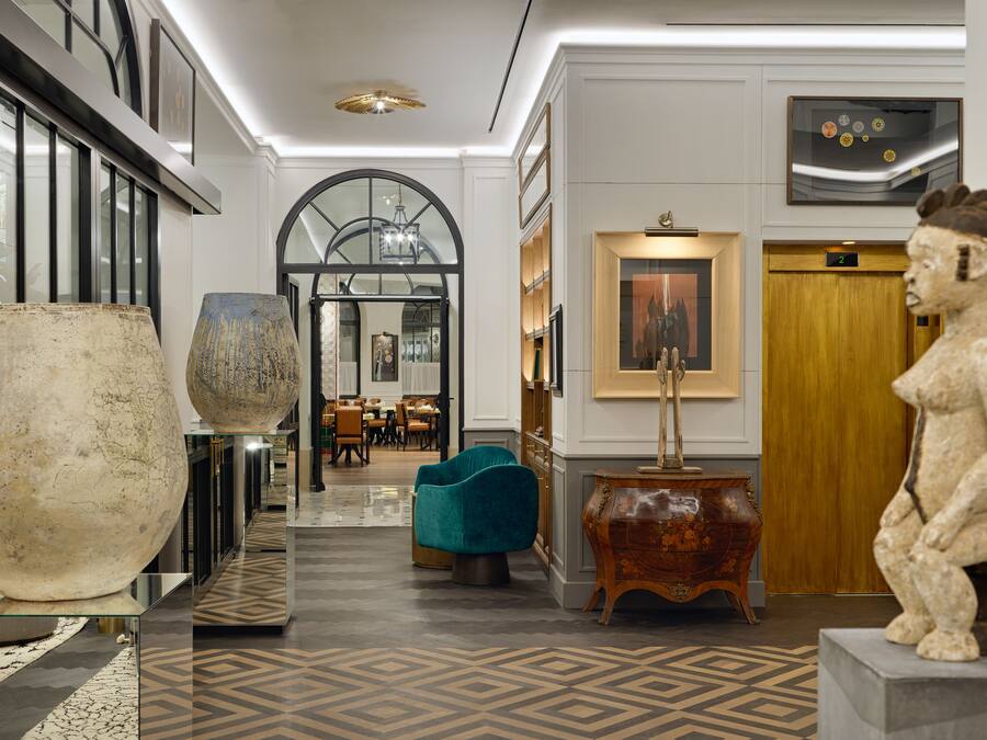 A lobby with a grand staircase, a large vase, a teal armchair, and a statue.