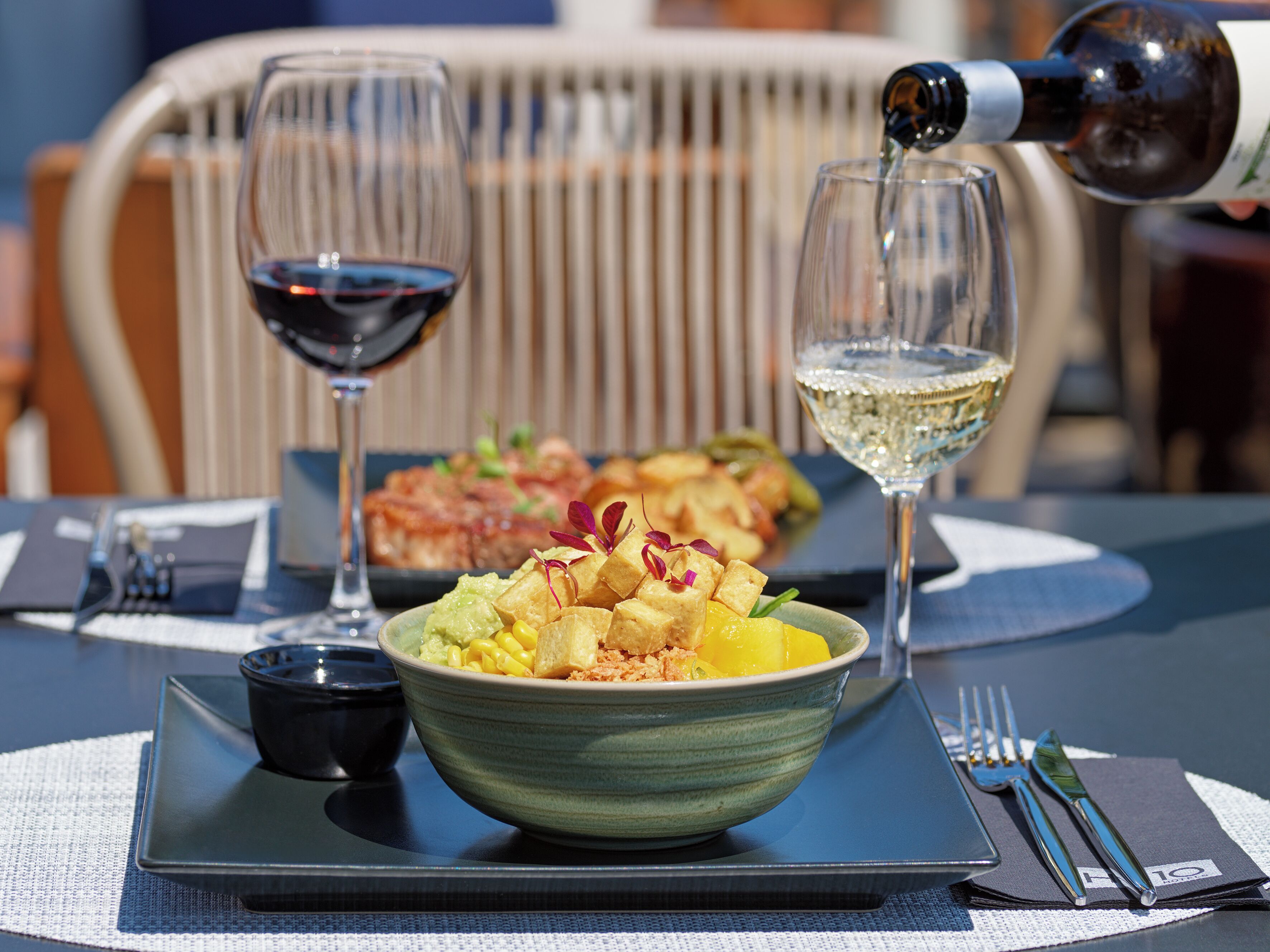 A dining table with a bowl of food, two wine glasses, and a bottle of wine.
