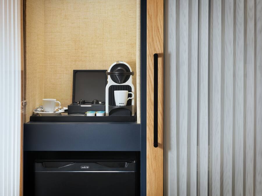 A compact kitchenette with a coffee maker, a cup, and a small refrigerator.