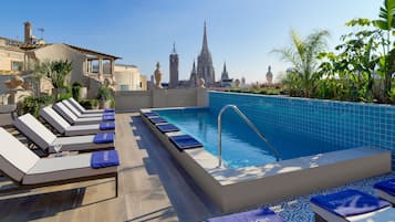 Zona de piscina en la azotea con sillones reclinables y vistas a una catedral.