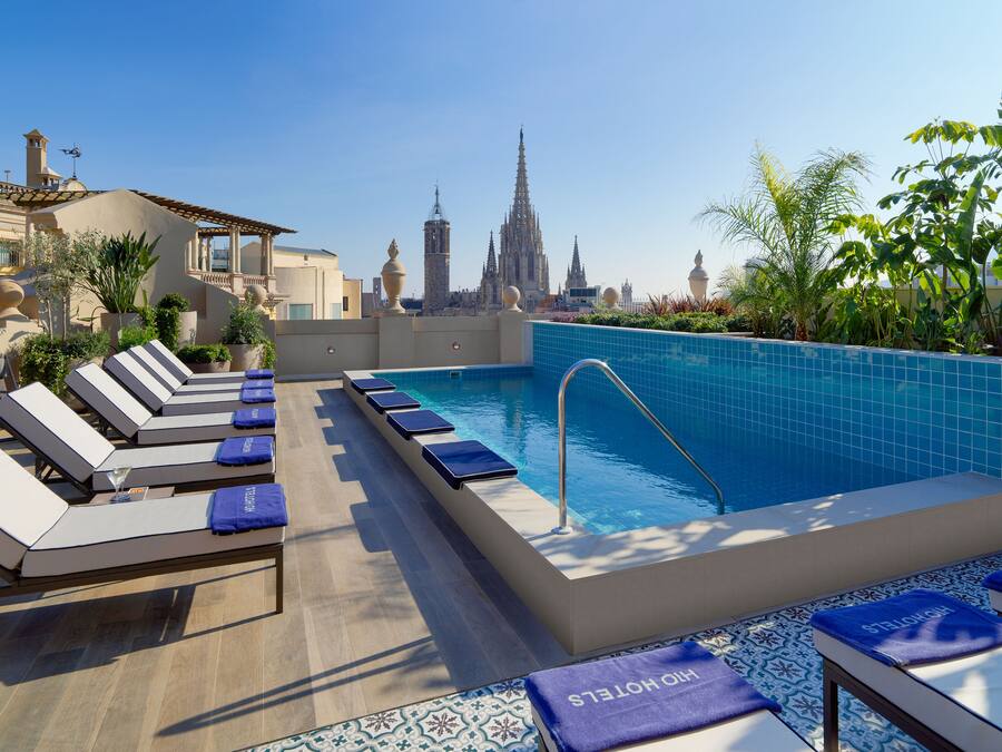 Zona de piscina en la azotea con sillones reclinables y vistas a una catedral.