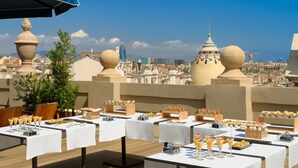 A rooftop dining area with tables set for breakfast, overlooking a cityscape with distinctive architecture. - H10 Madison (Barcelona)