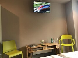 A hotel room with a bed, a wooden desk with a television mounted above it, and two chairs.