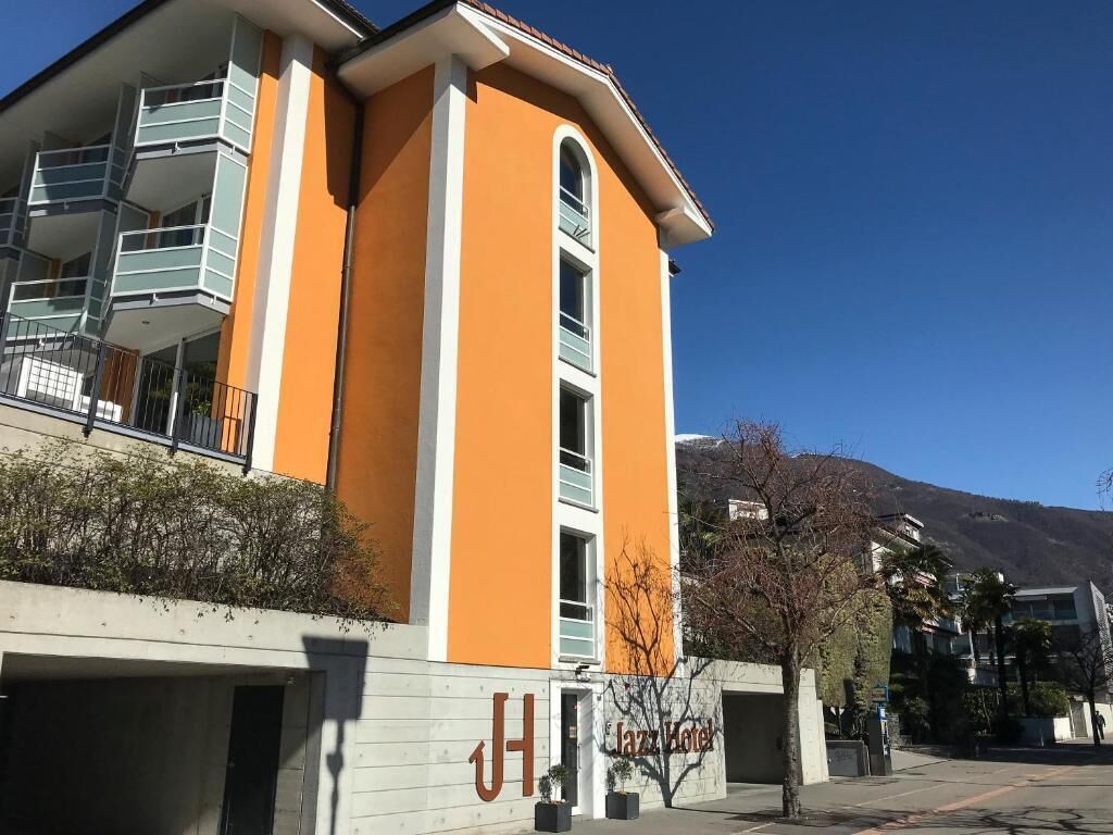 A building with a prominent 'J' sign, indicating a hotel. It features a modern design with a balcony on the upper floor.