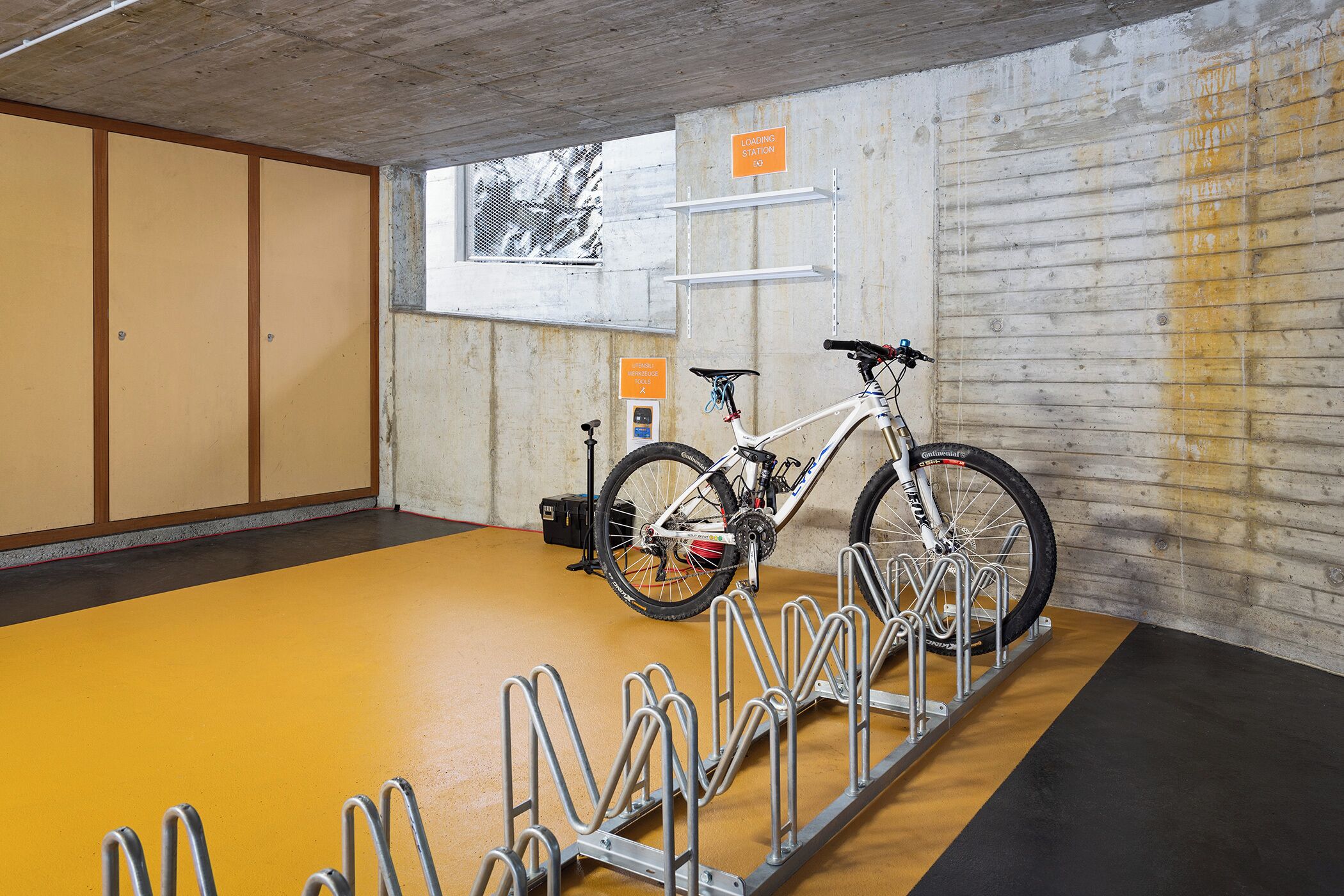 Un espace de stationnement pour vélos équipé d’un support à vélos et d’une fenêtre donnant sur des arbres.