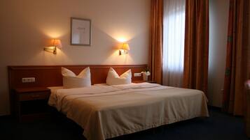Un cuarto de hotel con una cama grande, dos lámparas de noche, una mesita de noche y un cuadro enmarcado en la pared.