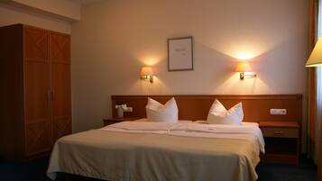 A hotel room with a large bed, two bedside lamps, a wooden wardrobe, and a framed picture on the wall.
