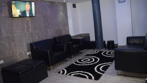 Un moderno espacio lounge con sofás de cuero negro, un tapete de diseño blanco y negro, un televisor montado en la pared y un reloj también en la pared.