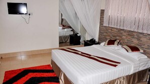 Una habitación de hotel con una cama, un televisor montado en la pared, una mesita de noche y otra mesita auxiliar.