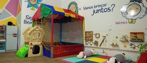 A children's playroom with a playhouse, a slide, and colorful mats.