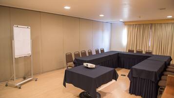 Un salón de conferencias con una larga mesa, sillas, una pizarra y un proyector.
