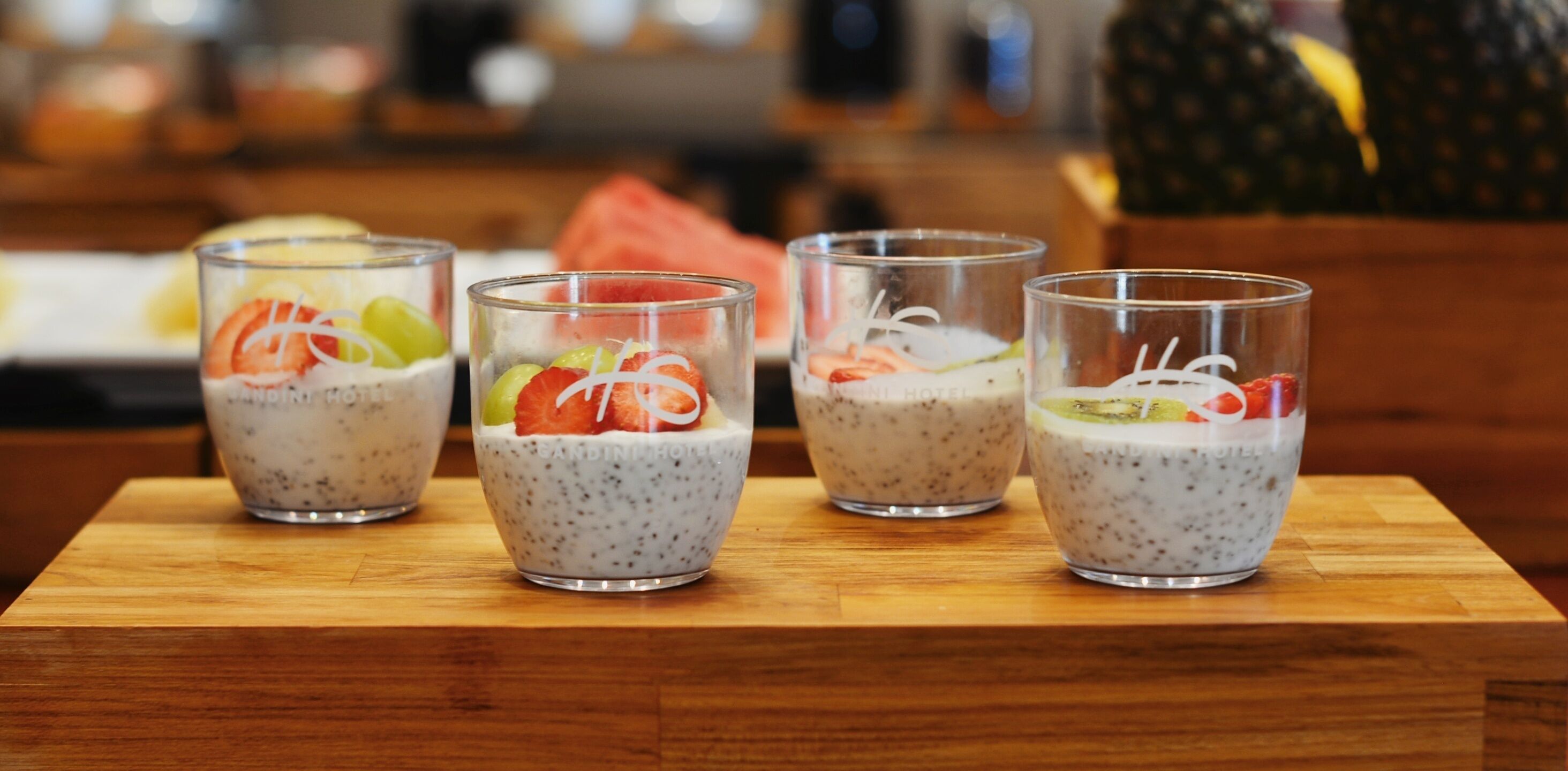 Cuatro vasos de pudín de chía con fruta sobre una mesa de madera.