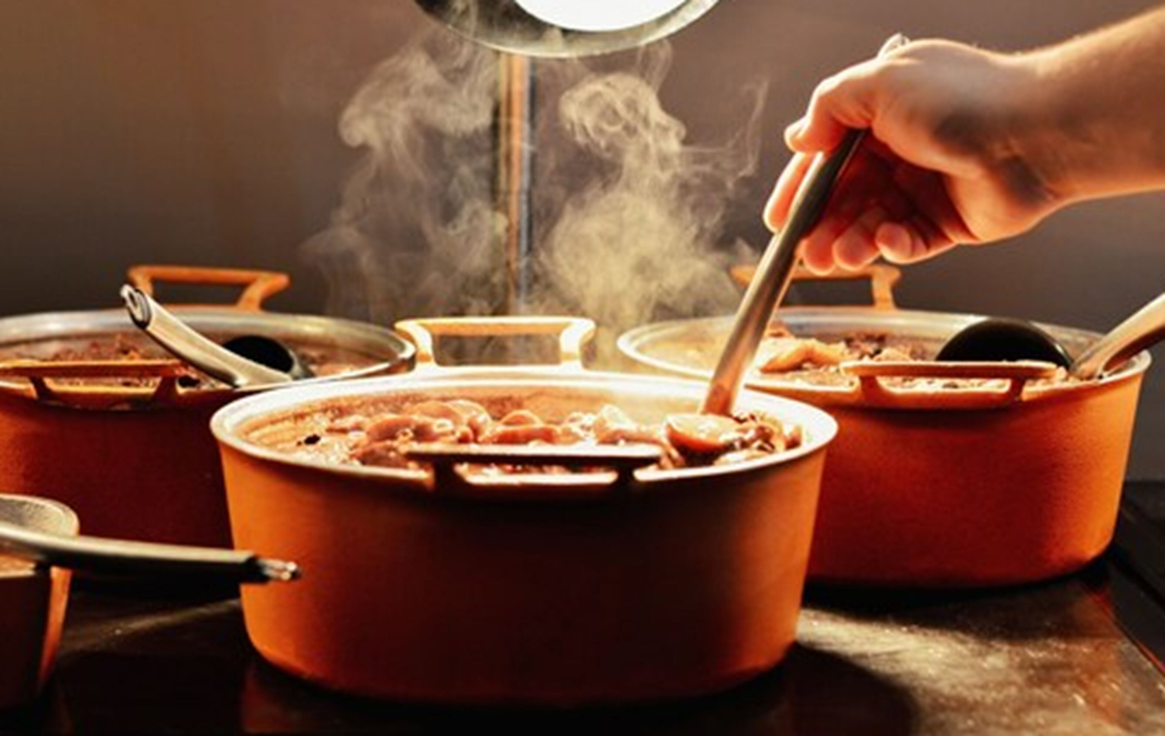 A person cooking with multiple pots on a stove, steam rising from the pots.