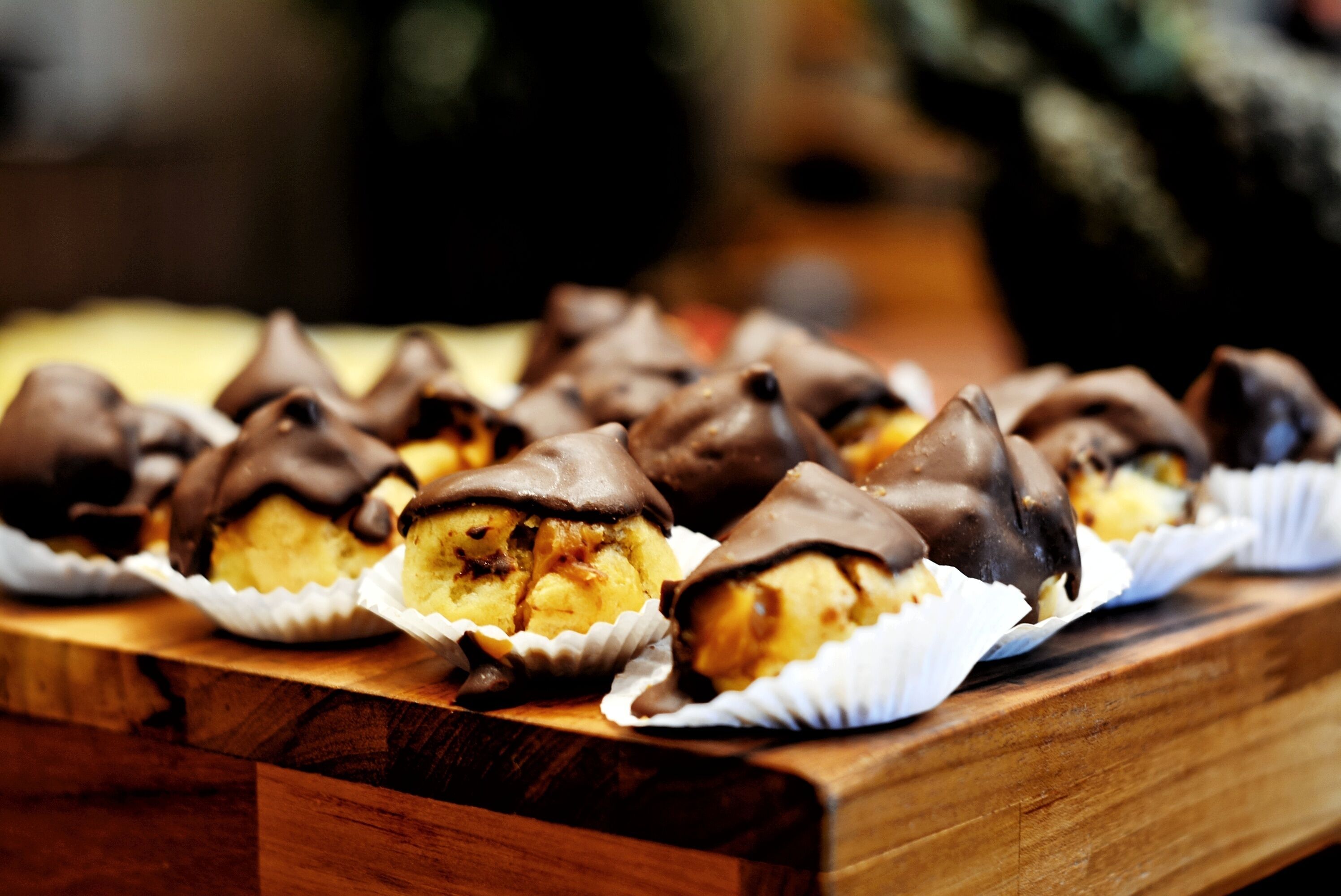 Ένα ξύλινο τραπέζι με διάφορα γλυκίσματα καλυμμένα με σοκολάτα, τοποθετημένα σε χάρτινα ποτηράκια.