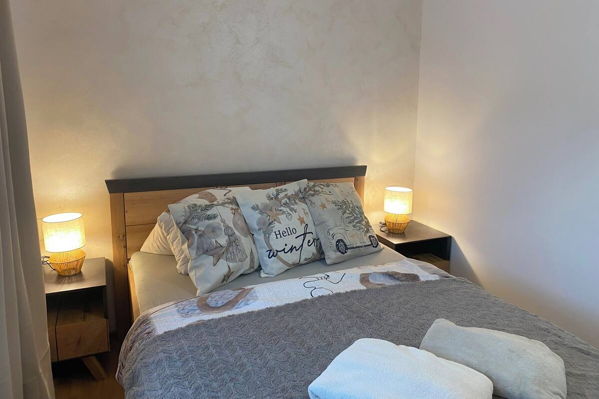Ein ordentlich gemachtes Bett mit dekorativen Kissen, einer Decke und zwei Nachttischlampen auf Holznachttischen.