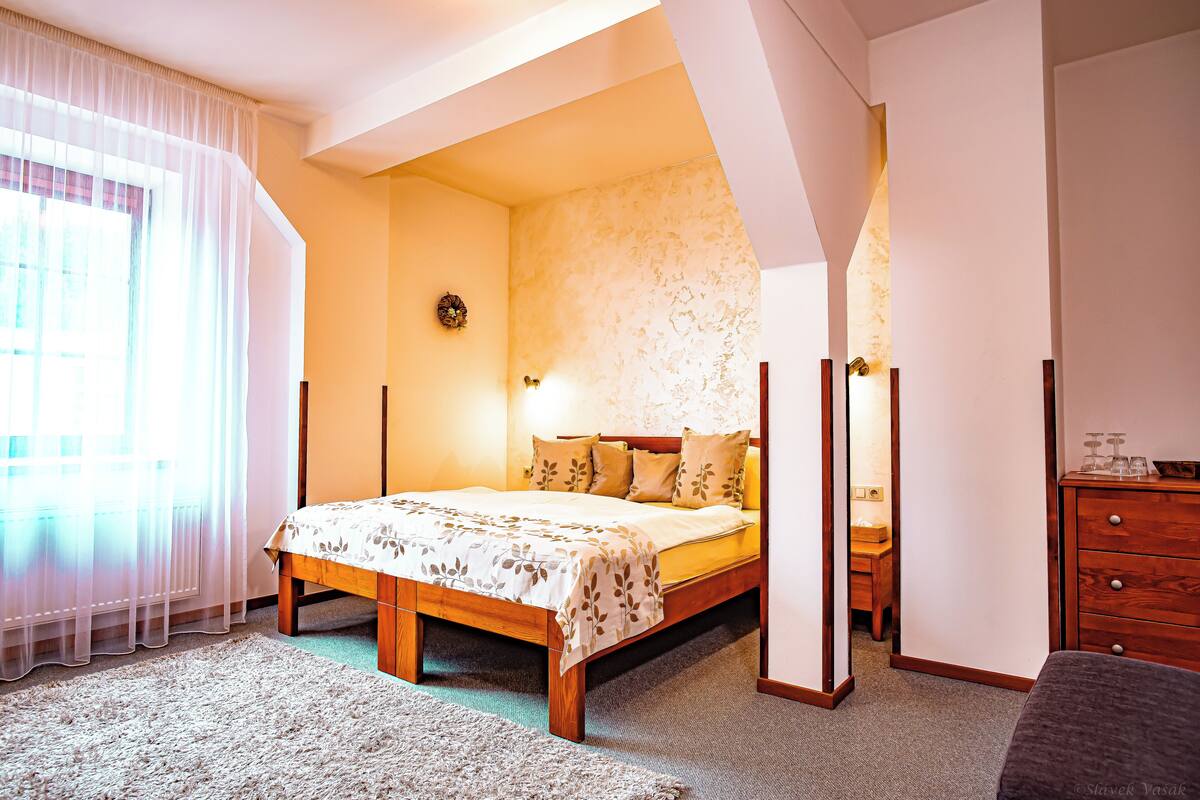 Ein Schlafzimmer mit einem hölzernen Bett, einem Nachttisch, einer Kommode und einem Fenster mit durchsichtigen Vorhängen.