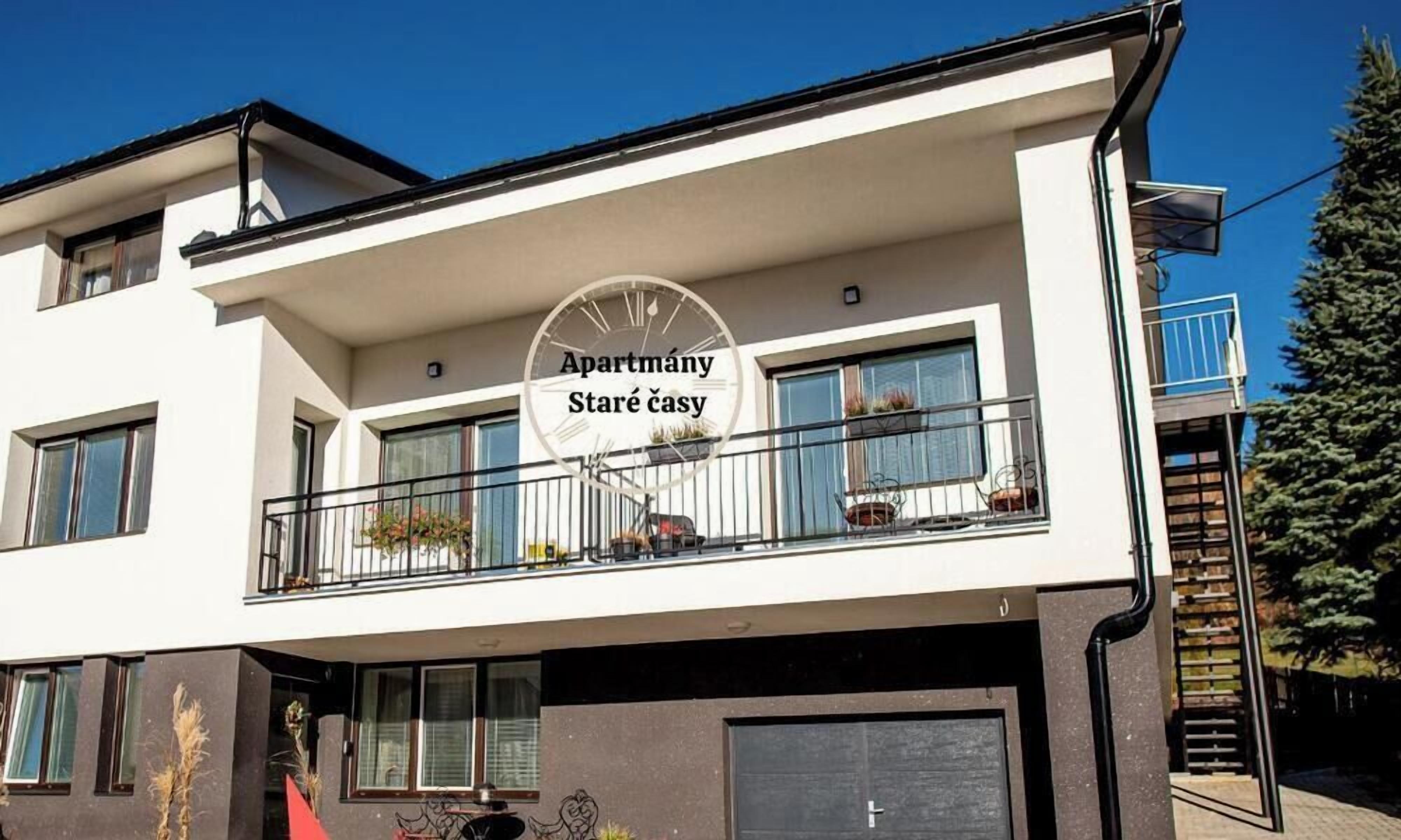 Un edificio de dos pisos con un balcón, un reloj y el texto 'Apartmány Staré časy' en la fachada.