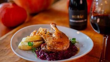 A plate with roasted chicken, potatoes, and red cabbage, accompanied by a bottle of wine and a glass of red wine on a wooden table.