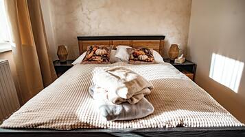 Una cama bien hecha con un edredón texturizado, dos almohadas con diseño de calabaza y una lámpara de noche sobre una mesita de madera.