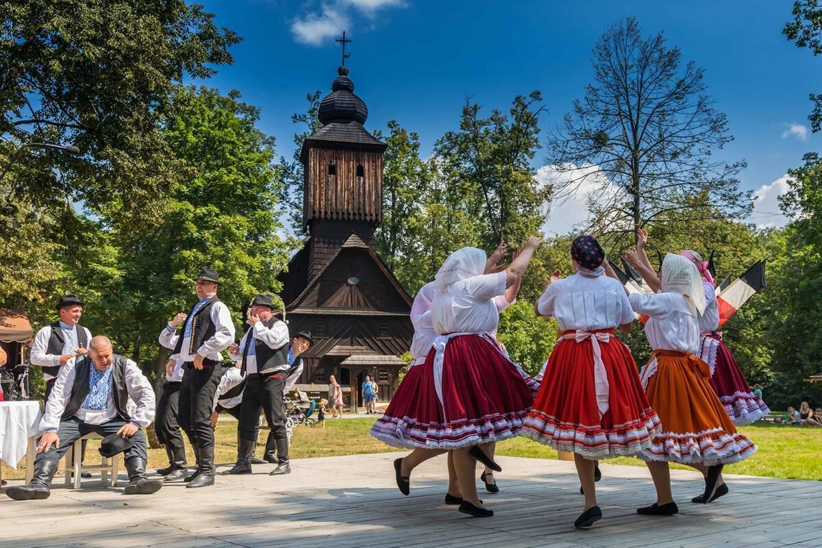 Eine traditionelle Tanzaufführung vor einer Kirche mit einem hölzernen Glockenturm.