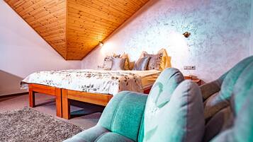 A bedroom with a wooden ceiling, a bed with patterned bedding, and a green armchair.