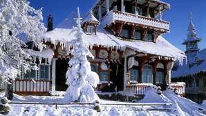 A multi-story building with a snow-covered roof and icicles, surrounded by snow-covered trees. - Penzion Staré časy (Horní Becva)