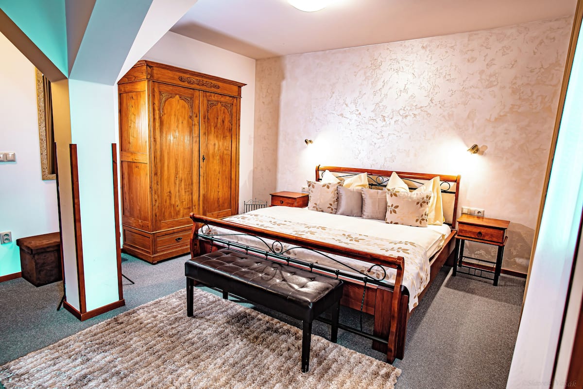 Ein Schlafzimmer mit einem großen Bett, einem Holzschrank, einer Bank und einem Nachttisch mit Lampe.