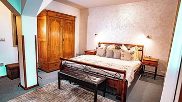 A bedroom with a large bed, a wooden wardrobe, a bench, and a nightstand with a lamp.