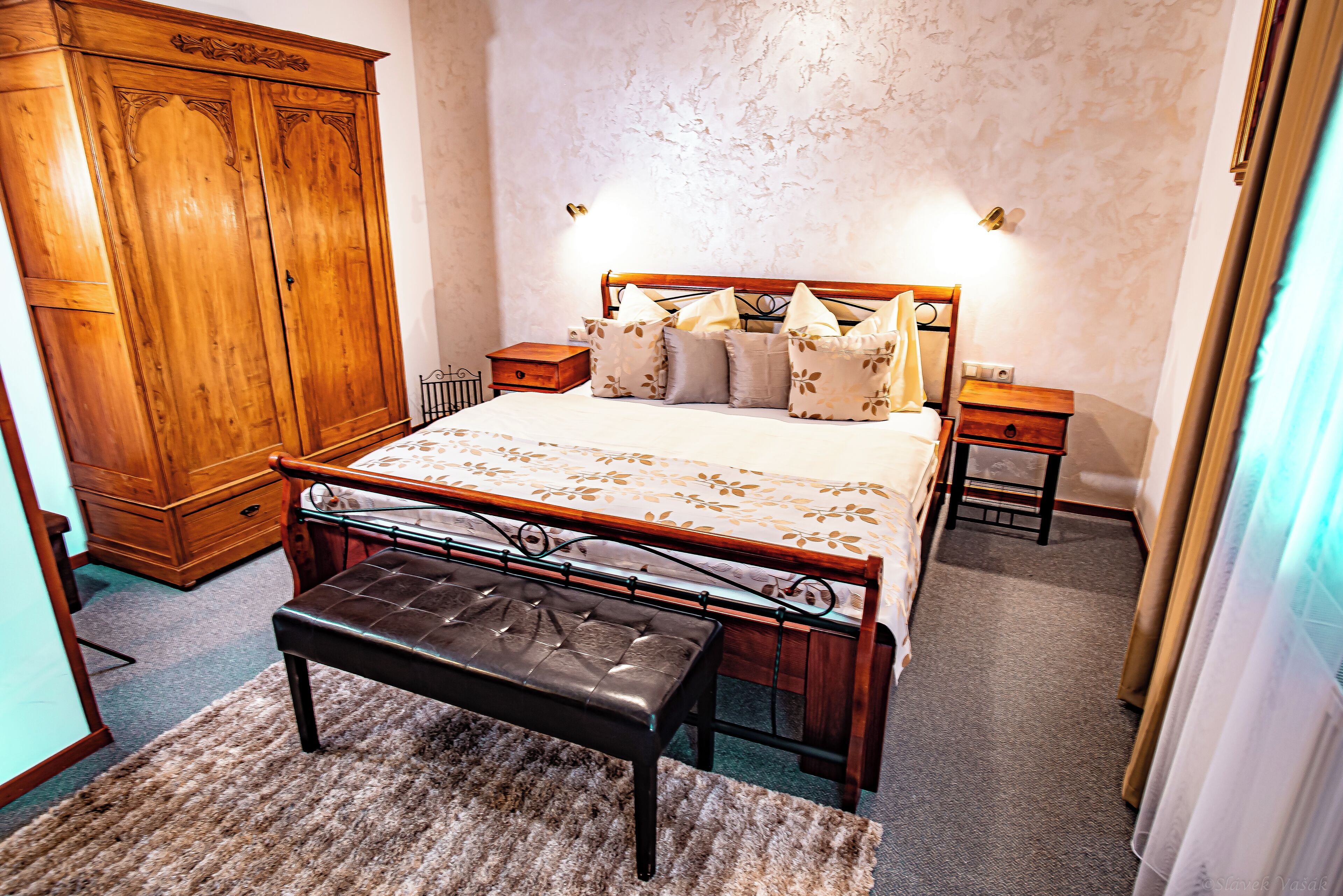 Un dormitorio con una cama de madera, un banco, un armario y una mesita de noche.