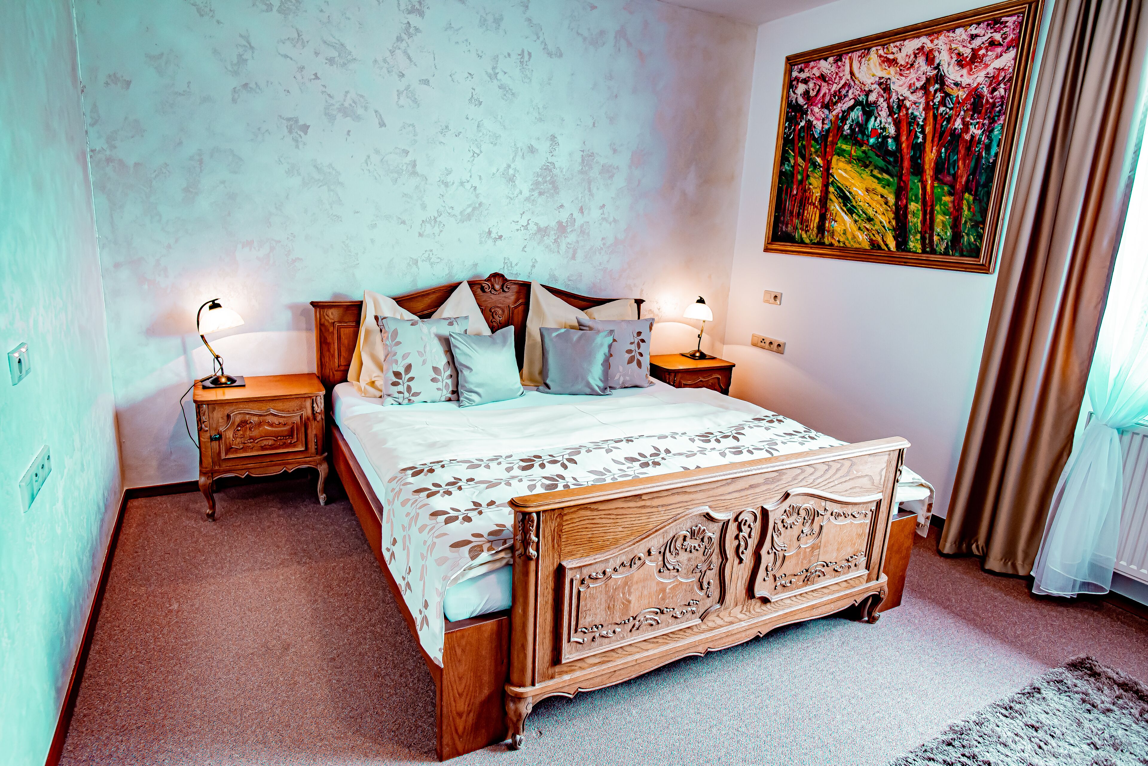 A bedroom with a wooden bed, two bedside tables, a nightstand, a floral-patterned bedspread, and a large painting on the wall.