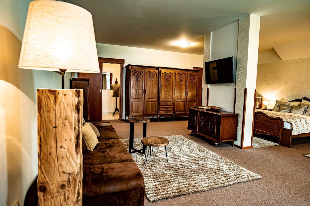 Ein Zimmer mit braunem Ledersofa, einem Holzkabinett, einem an der Wand montierten Fernseher und einem Bett mit Kopfteil.