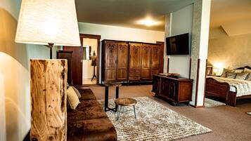 A room with a brown leather sofa, a wooden cabinet, a television mounted on the wall, and a bed with a headboard.