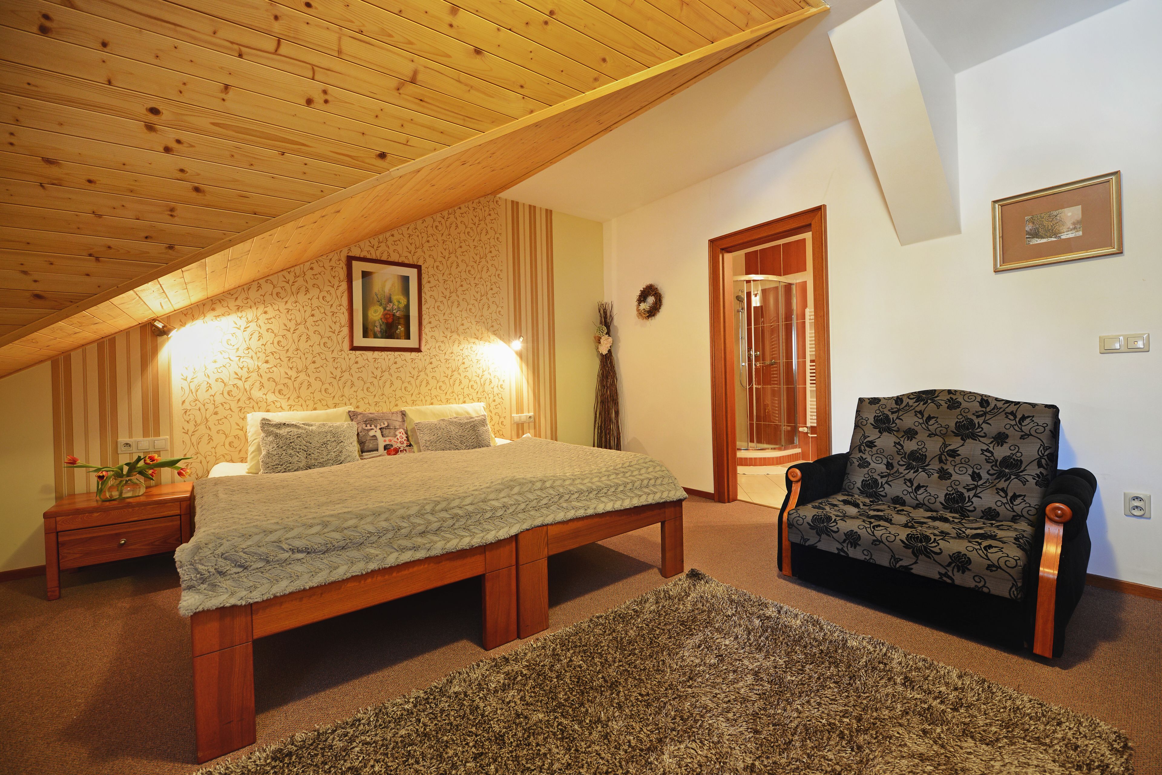 A bedroom with a wooden ceiling, a bed, a chair, and a nightstand.