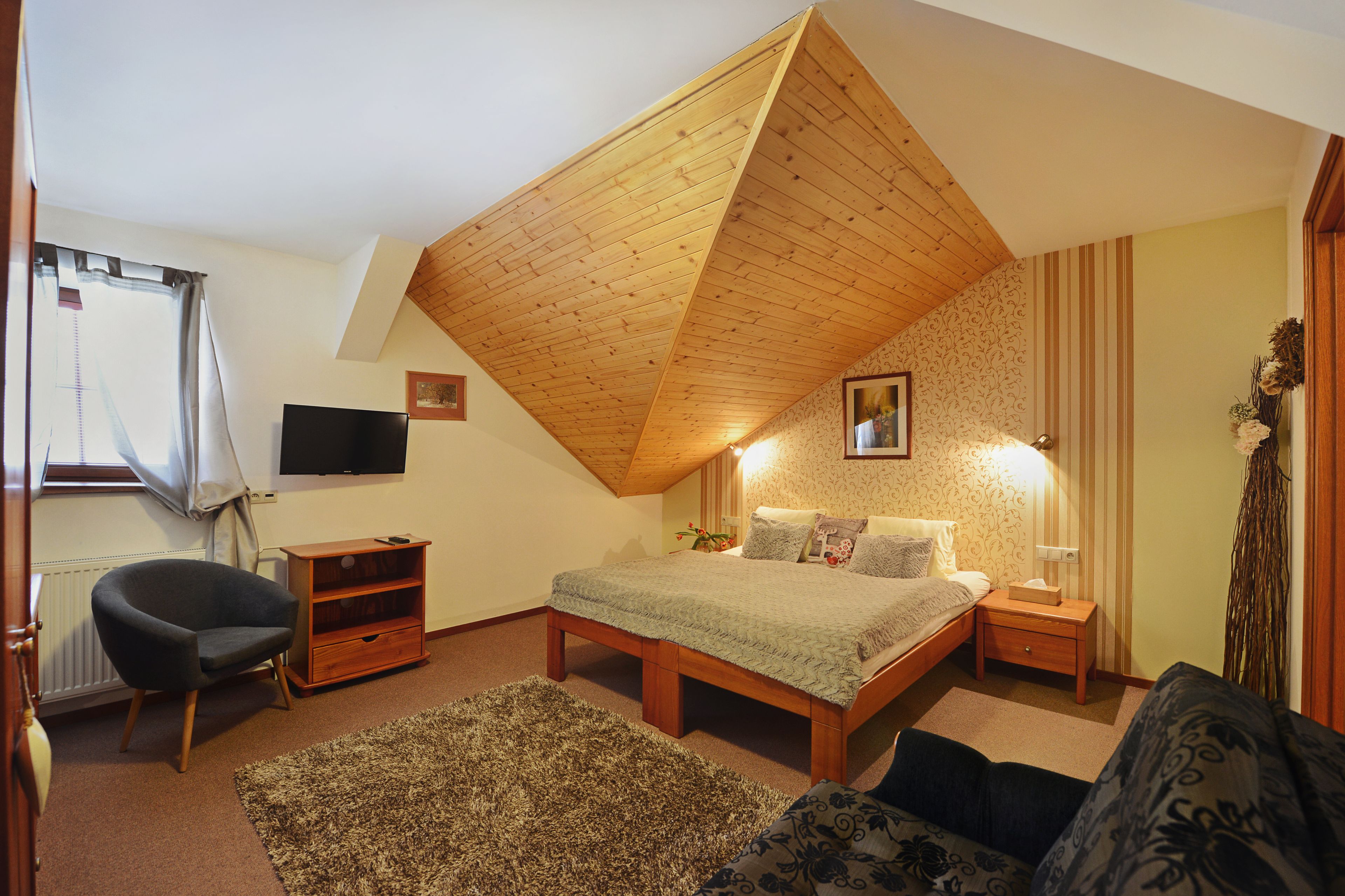 A bedroom with a sloped ceiling, a bed, a chair, a TV, and a small table.