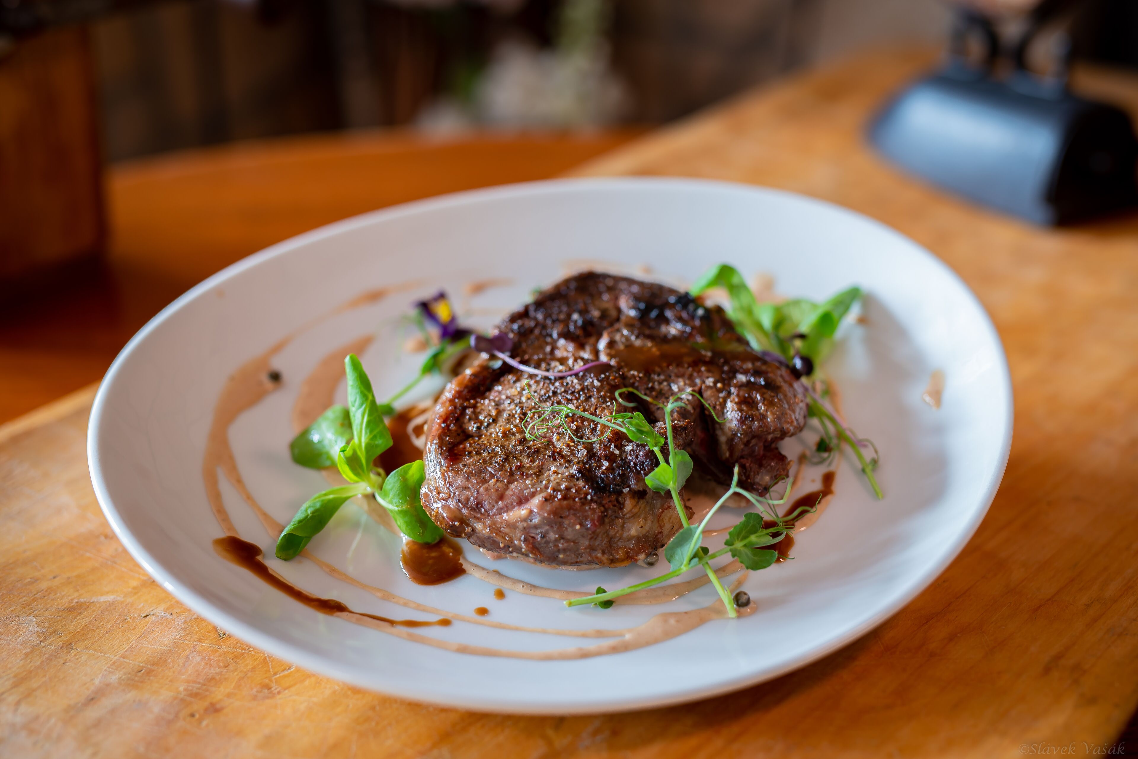 A plate of steak with greens and sauce on a wooden table.