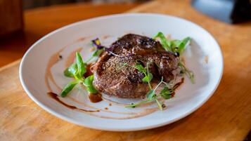 A plate of steak with greens and sauce on a wooden table.
