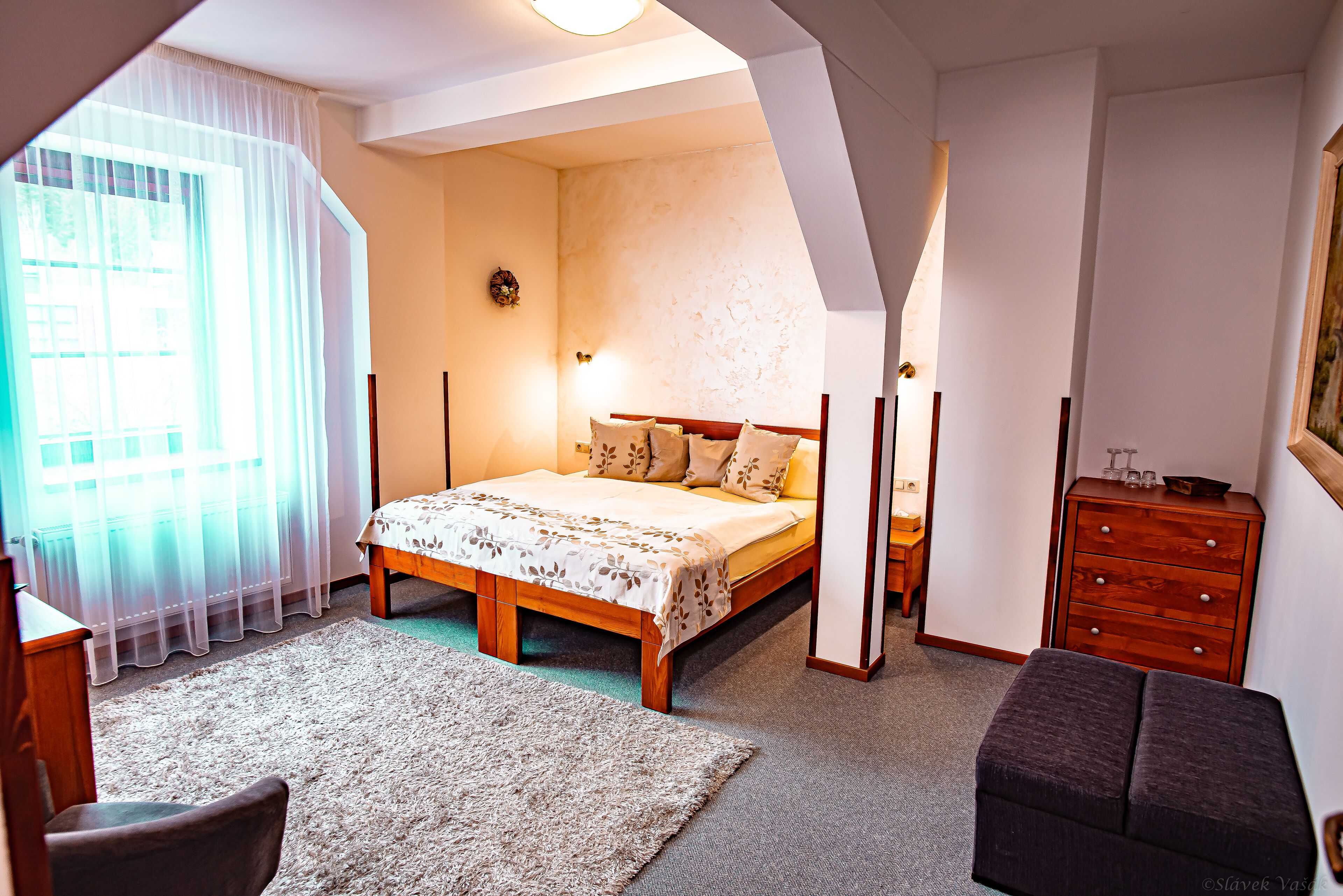 Un dormitorio con una cama, un aparador, una silla y una ventana con cortinas traslúcidas.