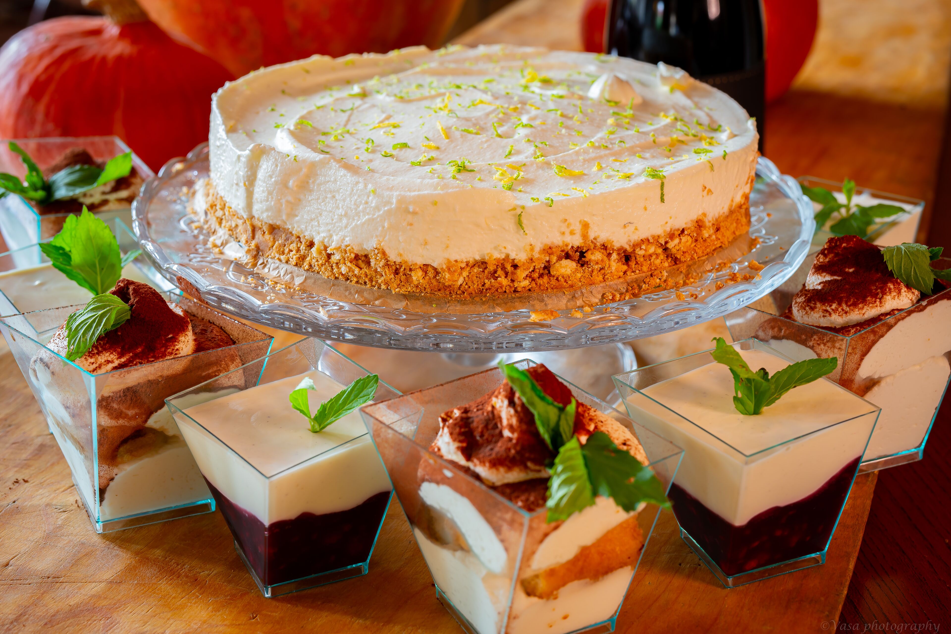 Een dessertbuffet met een cheesecake op een glazen plateau, omringd door diverse desserts in glazen recipiënten.