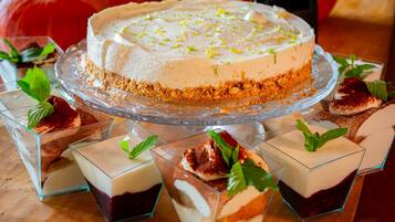 Een dessertbuffet met een cheesecake op een glazen plateau, omringd door diverse desserts in glazen recipiënten.