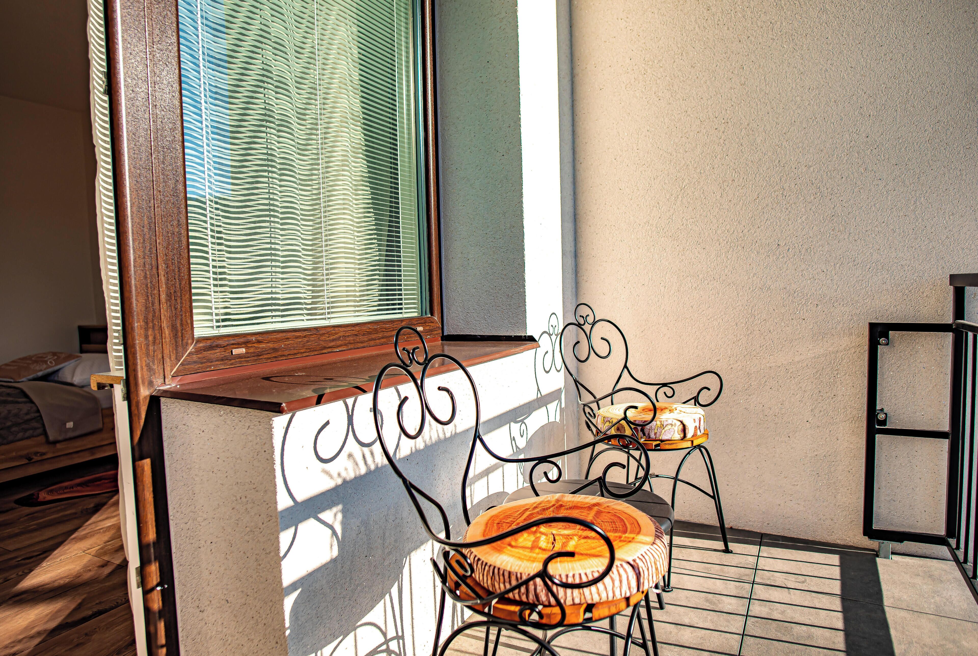 A balcony with a metal chair and a small table, a window with blinds, and a door.