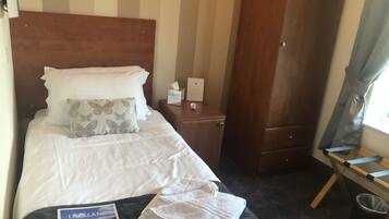 Quarto de hotel com cama, mesa de cabeceira, guarda-roupa de madeira, janela com cortinas e pequena mesa com toalha e controle remoto.