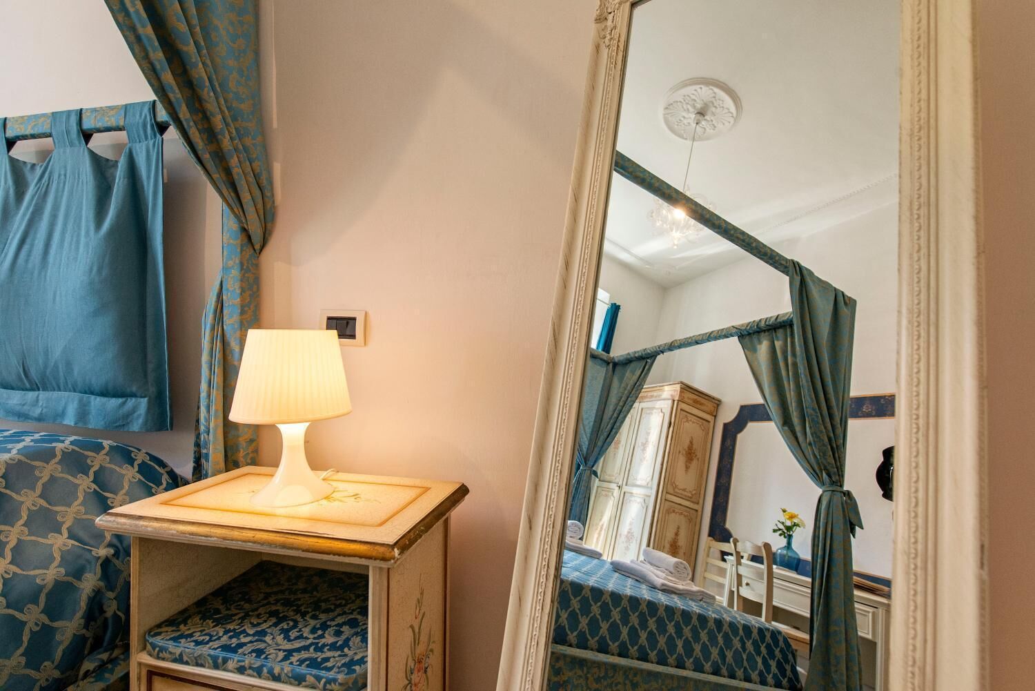 A room with a bed, a bedside table with a lamp, a mirror, and a wardrobe.