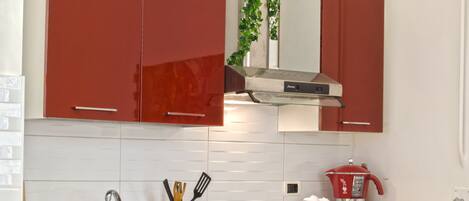 A modern kitchen with red cabinets, a stainless steel range hood, and a countertop with a basket of groceries and a bottle of wine.