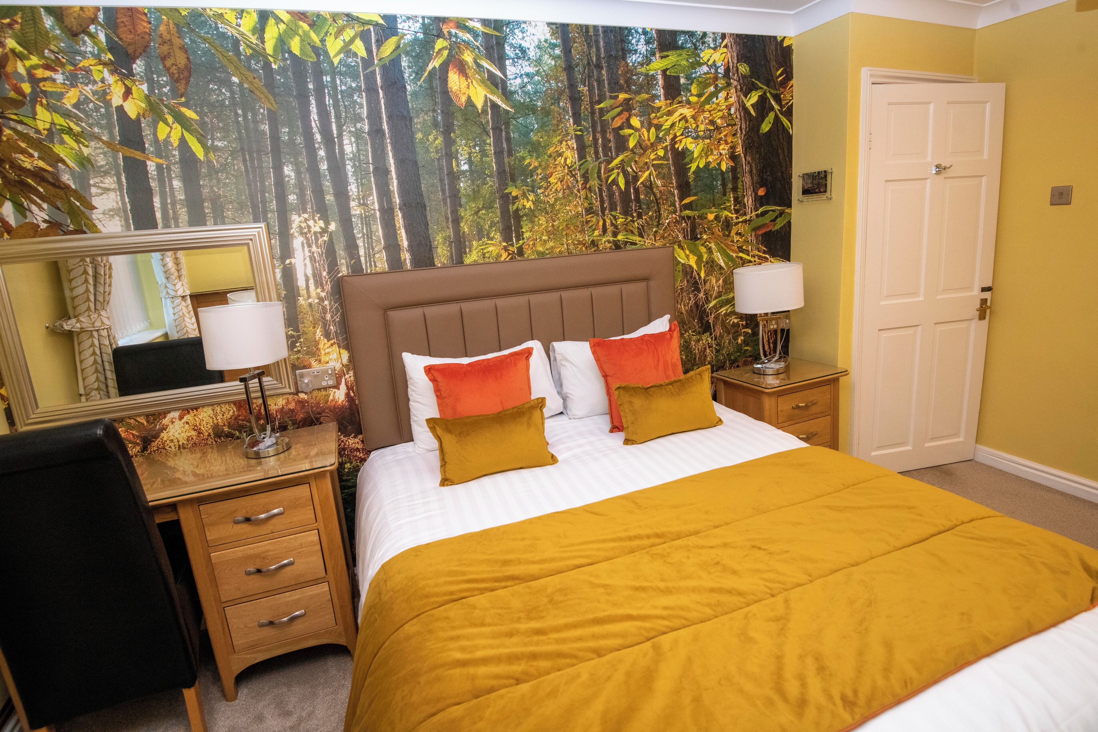 Un dormitorio con cama, mesita de noche, cómoda, espejo y puerta.
