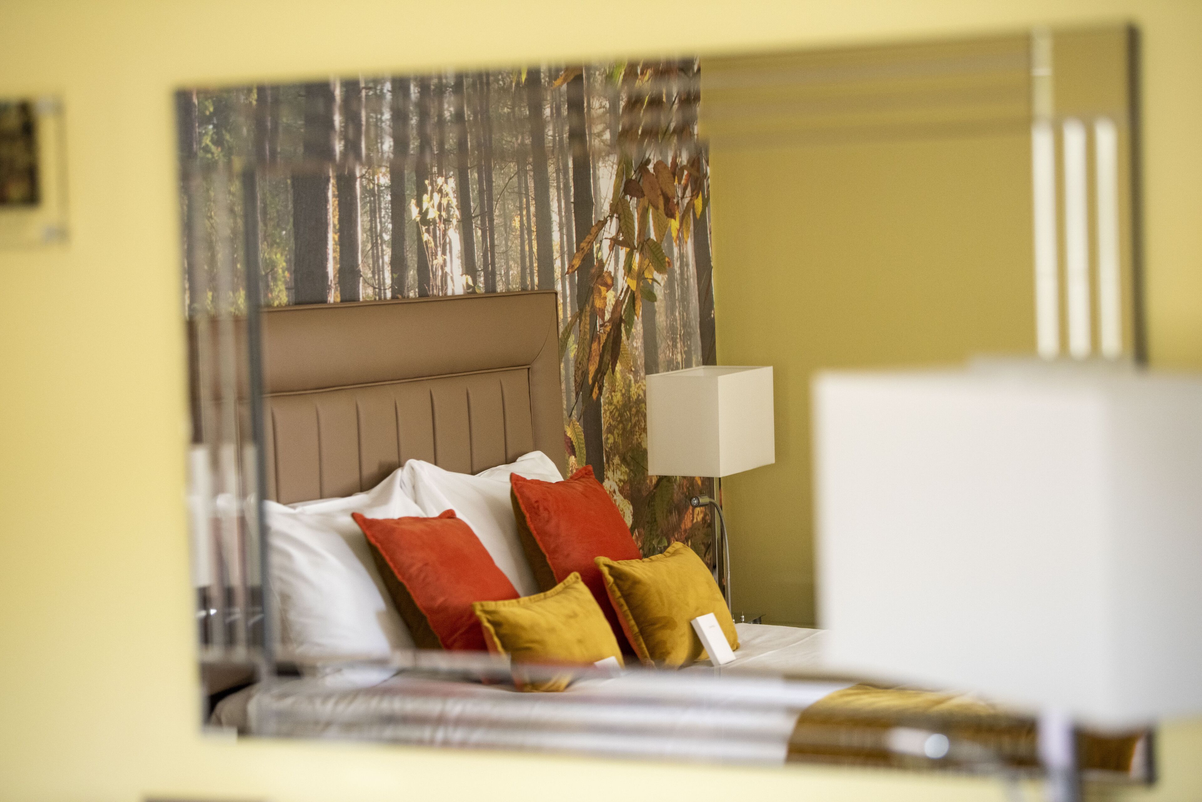 Una habitación de hotel con cama, almohadas, mesita de noche y lámpara.