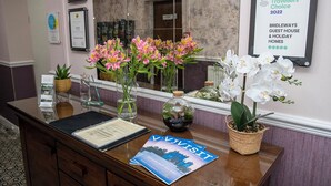 Mostrador de recepción con una placa de TripAdvisor, un folleto y flores decorativas.