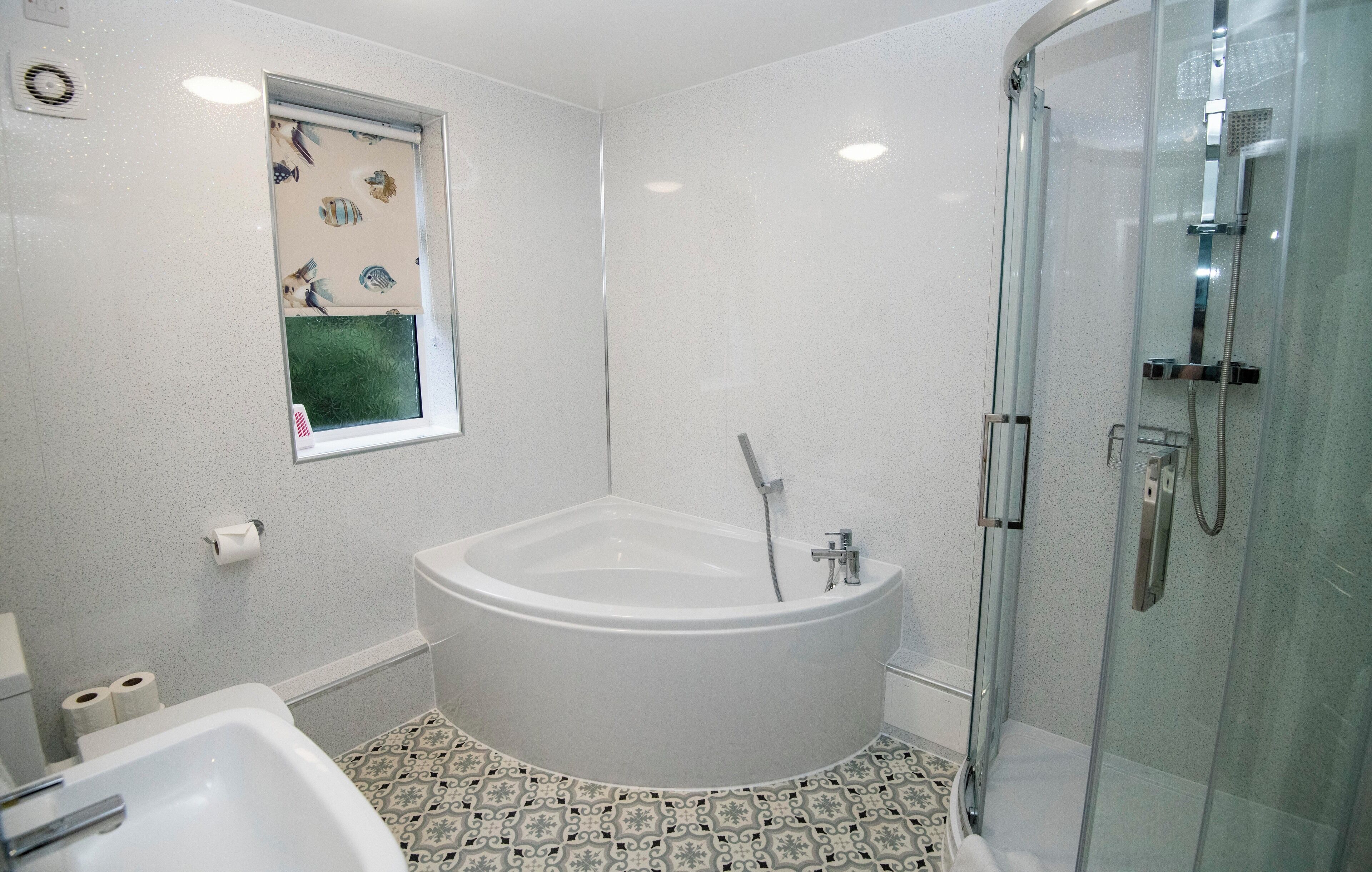 Un baño con bañera independiente, cabina de ducha de vidrio y baldosas de suelo estampadas.