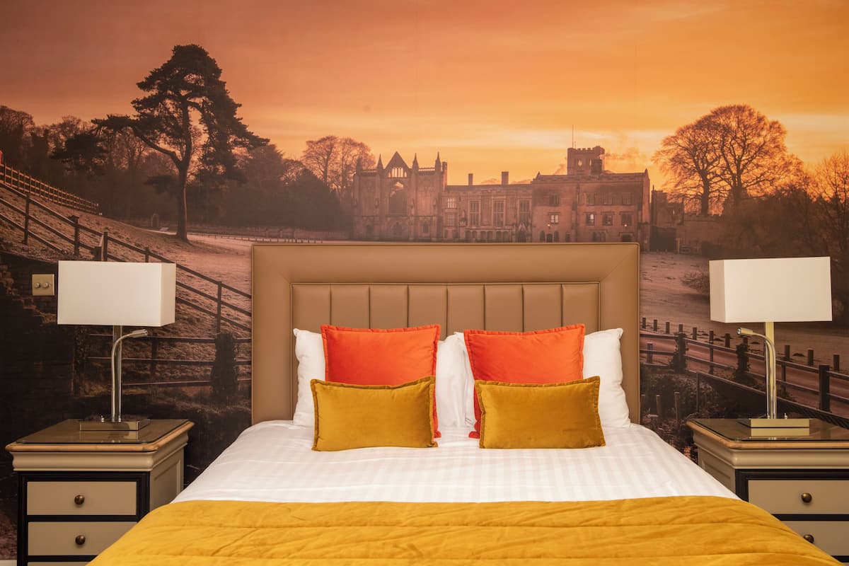 Een hotelkamer met een bed, twee nachtkastjes en een muurschildering van een historisch gebouw.