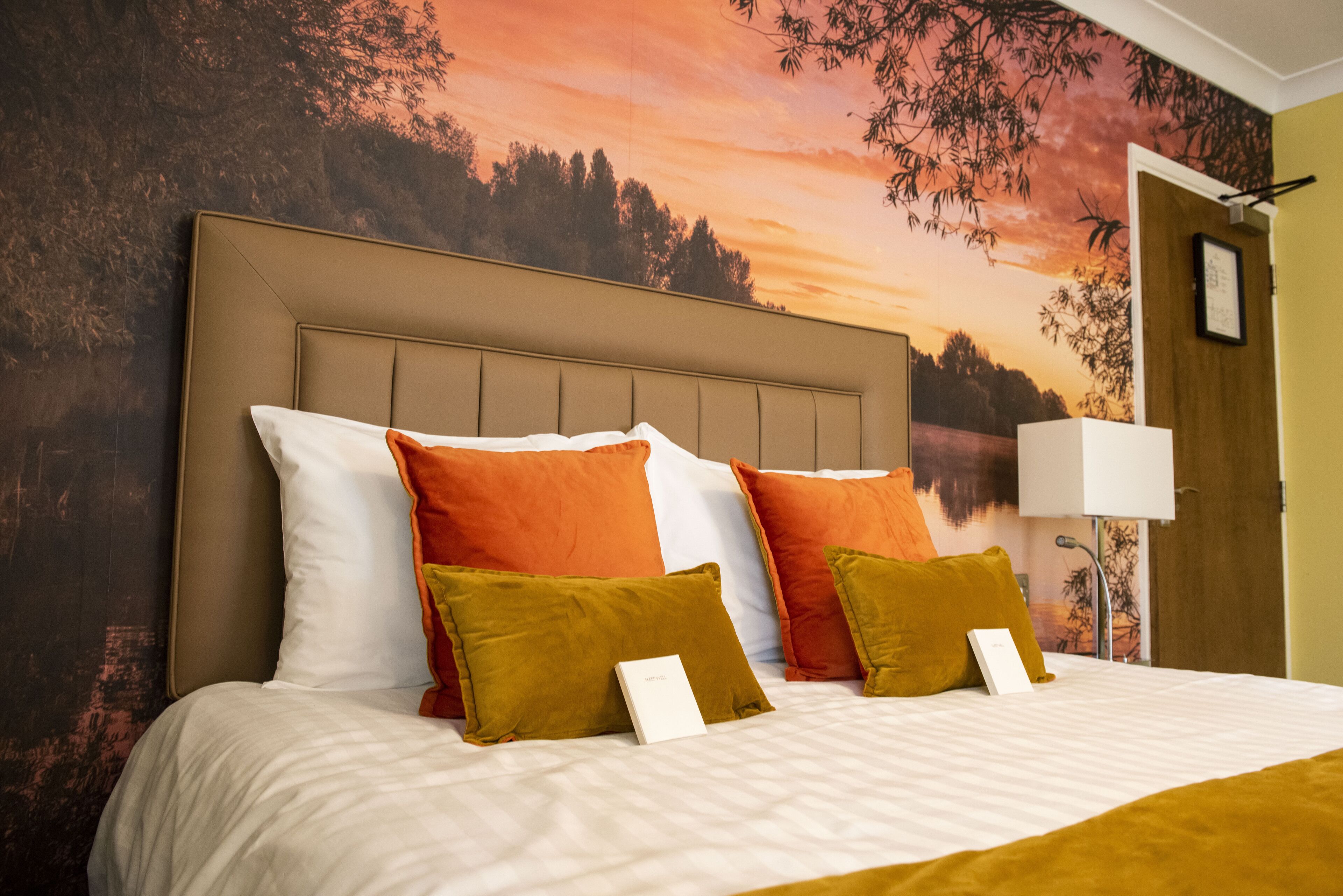 A neatly made bed with a headboard, multiple pillows, and a framed picture on the wall.